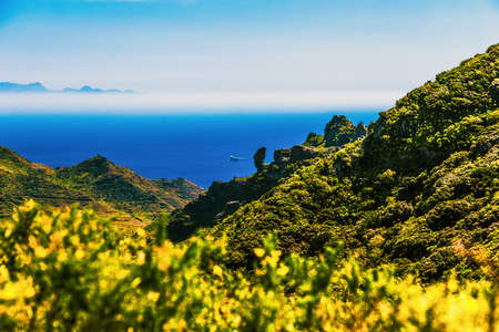 Coast or shore of Atlantic ocean with green mountain or rock and sky with horizon and island at background in Tenerife Canary island, Spain at spring or summerの写真素材