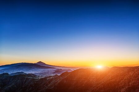Sun with sunlight over mountains on blue sky with fog and Teide volcano on background at evening sunset in Tenerife Canary island, Spainの写真素材