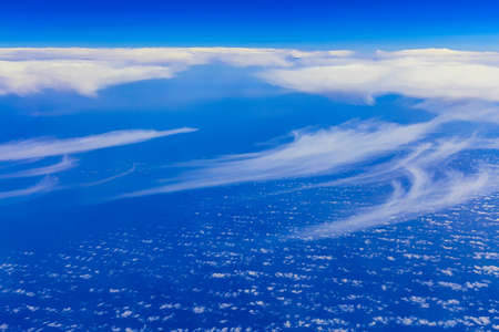 View on blue sky above white clouds from the window of plane with horizon and skyline over oceanの写真素材