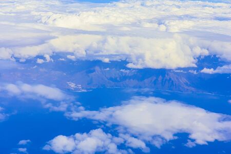 View on blue sky above white clouds or cloudscape from plane above island in oceanの写真素材