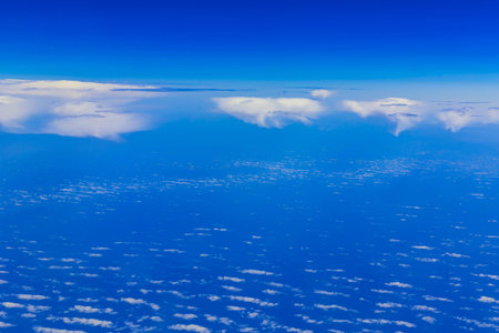 View on blue sky above white clouds from the window of aircraft with skyline above ocean