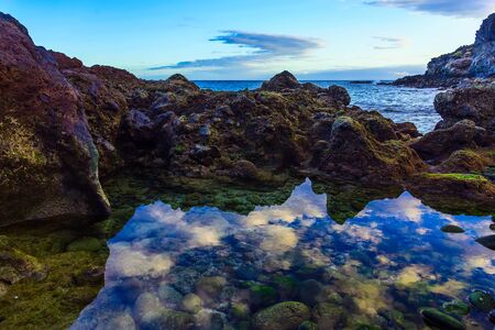 Stone Shore of Atlantic Ocean with Sky Reflection in water on Tenerife Islandの写真素材