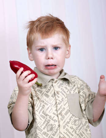 The sad little boy holds red pepper in a handの写真素材
