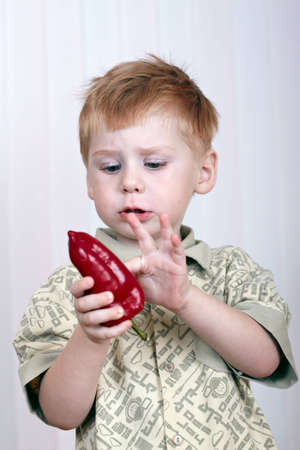 The sad little boy holds red pepper in a handの写真素材