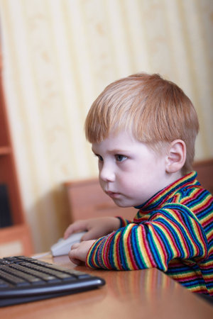 The little boy plays on a computer in a room