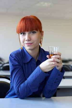 The student on employment sits at a table and holds in hands a glass with tea