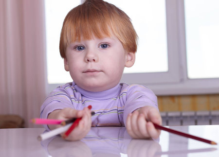 The little boy sits at a table with pencils in handsの写真素材