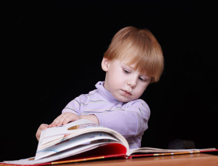 boy with the book behind a table on the black background