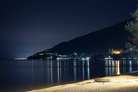 Night beach of sand and pebbles, Abkhazia Gagra. Fishing boat boat lies on the shore. The light of the city lights, high mountains, travel, tourism, flying stars.の写真素材