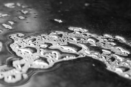 Rain water on a smooth black surface macro shot. Drops of water on the surface close-up.の写真素材