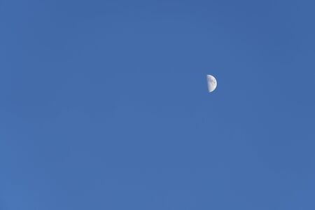 Half moon on a blue sky. Earth satellite in the afternoon on blue sky.の写真素材