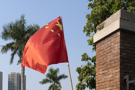 The red flag of the Republic of China flutters in the wind. Flag with yellow stars on a background of palm trees and blue sky. Six flagpole made of bamboo.の写真素材
