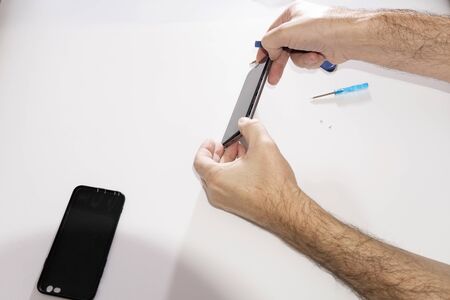 Phone repair in a service center. Dismantling glass from a mobile phone. Replacing the touchpad matrix of the glass touchpad. Hands repair the phone.の写真素材