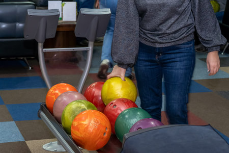 A hand holds a colored bowling ball. Wooden walkway in a bowling alley. Game with balls. Girl takes...