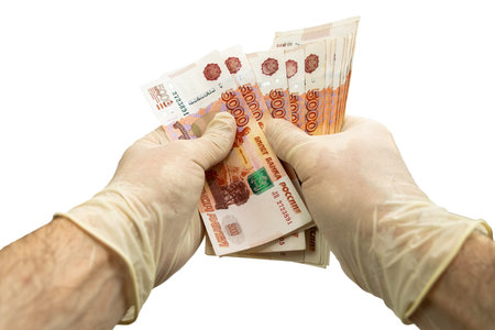Two hands in white medical protective gloves are counting a bundle of notes with a face value of...