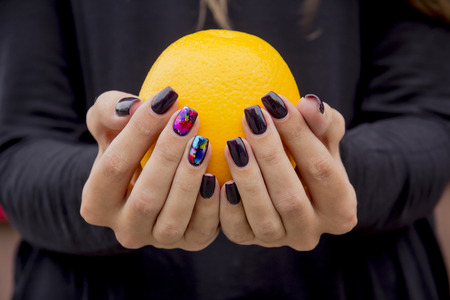 Bright, fresh orange in the hands of the girl with the fashionable manicureの写真素材