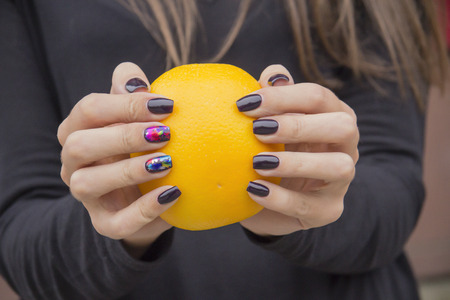 Bright, fresh orange in the hands of the girl with the fashionable manicureの写真素材