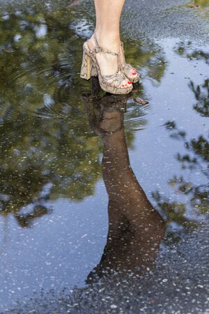 Close-up of women's legs in fashionable shoes and their reflection in a puddleの写真素材