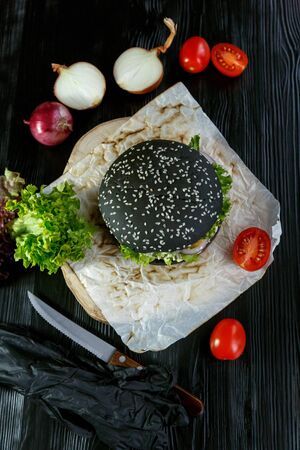 Black burger with tomatoes, with Chinese cabbage, onions on a black wooden backgroundの写真素材