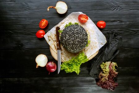 Black burger with tomatoes, with Chinese cabbage, onions on a black wooden backgroundの写真素材