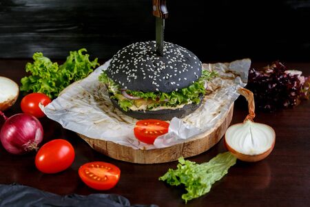 Black burger with tomatoes, with Chinese cabbage, onions on a black wooden backgroundの写真素材