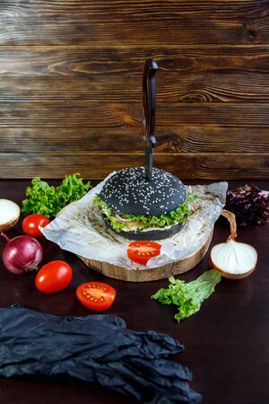 Black burger with tomatoes, with Chinese cabbage, onions on a black wooden backgroundの写真素材