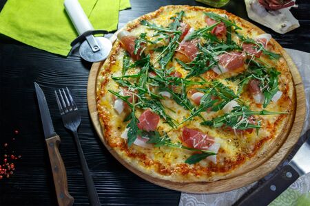 Pizza with bacon, cheese and herbs on a wooden dish on a black wooden backgroundの写真素材