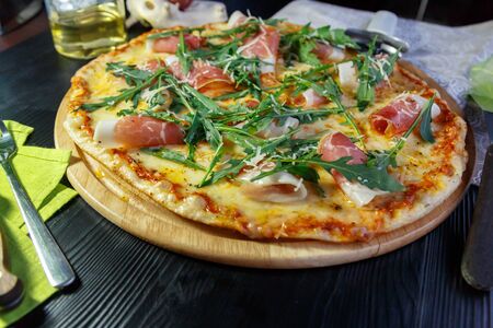 Pizza with bacon, cheese and herbs on a wooden dish on a black wooden backgroundの写真素材