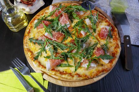 Pizza with bacon, cheese and herbs on a wooden dish on a black wooden backgroundの写真素材
