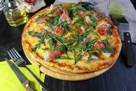 Pizza with bacon, cheese and herbs on a wooden dish on a black wooden backgroundの写真素材