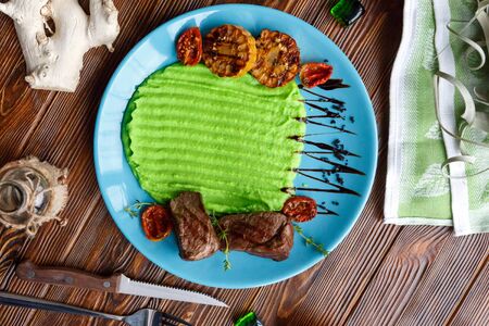Meat with a side dish of mashed potatoes, bread, a knife and a fork on a plate on a wooden brown backgroundの写真素材