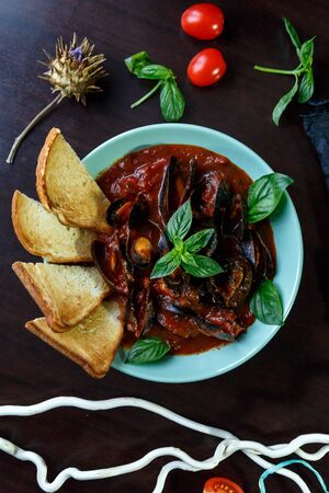 Mussels in tomato sauce with garlic in a blue plate on a brown wooden backgroundの写真素材