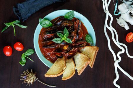Mussels in tomato sauce with garlic in a blue plate on a brown wooden backgroundの写真素材
