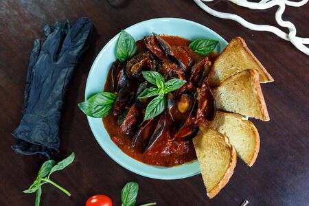 Mussels in tomato sauce with garlic in a blue plate on a brown wooden backgroundの写真素材