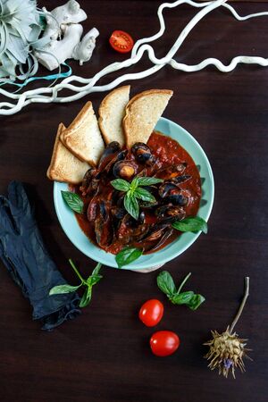 Mussels in tomato sauce with garlic in a blue plate on a brown wooden backgroundの写真素材