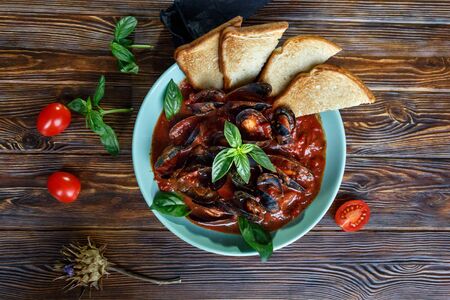 Mussels in tomato sauce with garlic in a blue plate on a brown wooden backgroundの写真素材