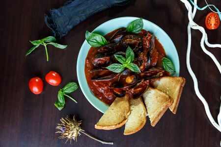 Mussels in tomato sauce with garlic in a blue plate on a brown wooden backgroundの写真素材