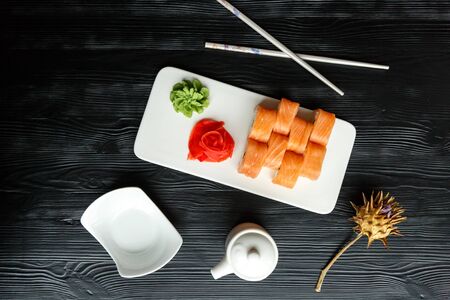 Appetizing sushi Japanese dish of salmon and rice with red and green pasta on a white kitchen board with Japanese chopsticks and sauceboats on a black wooden backgroundの写真素材