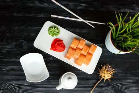 Appetizing sushi Japanese dish of salmon and rice with red and green pasta on a white kitchen board with Japanese chopsticks and sauceboats on a black wooden backgroundの写真素材