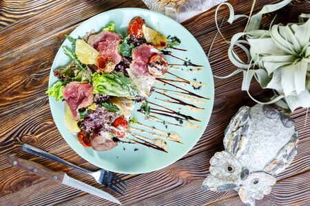Pork meat medallions with vegetables and herbs on a blue plate on a wooden backgroundの写真素材