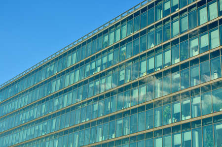 Glass facade of modern office building with reflection of blue sky and clouds.のeditorial素材