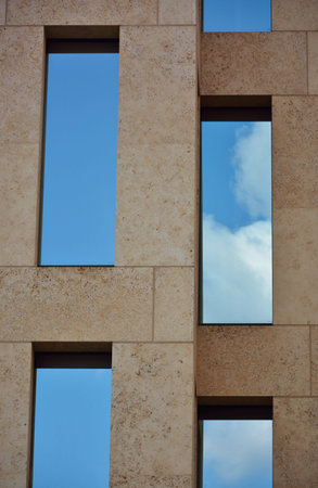 Detail of glass facade of modern office building with reflection of blue sky and clouds.