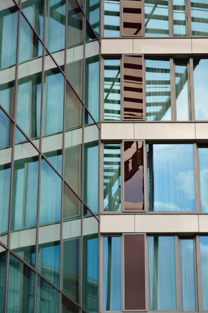 Detail of glass facade of modern office building with reflection of blue sky and clouds.