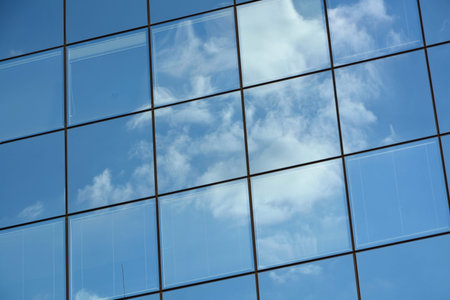 Detail of glass facade of modern office building with reflection of blue sky and clouds.