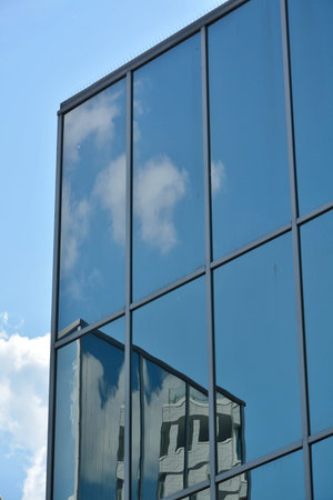 Detail of glass facade of modern office building with reflection of blue sky and clouds.
