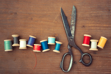 Old scissors and wooden spools of colored thread lie on a wooden tableの写真素材