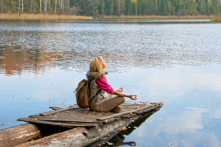 Girl with a backpack meditates on the lakeの写真素材