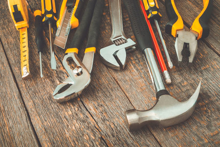 Hammer, screwdriver, pliers, a knife, a key and a red pencil lying on a wooden board
