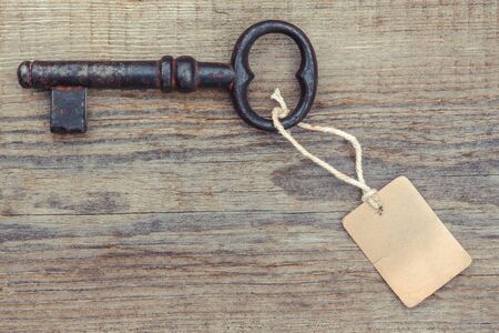 Old rusty key with a paper label lies on a wooden boardの写真素材