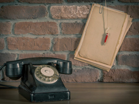 Old telephone and paper with a pencil on a background of a brick wall